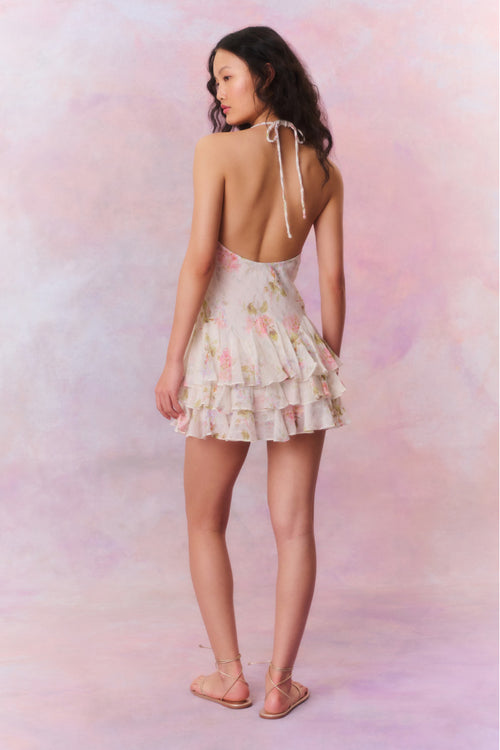 Large-scale floral printed mini dress beginning with twisted braided straps you can tie for a halter. Asymmetrical seams line the piece above a handkerchief skirt.