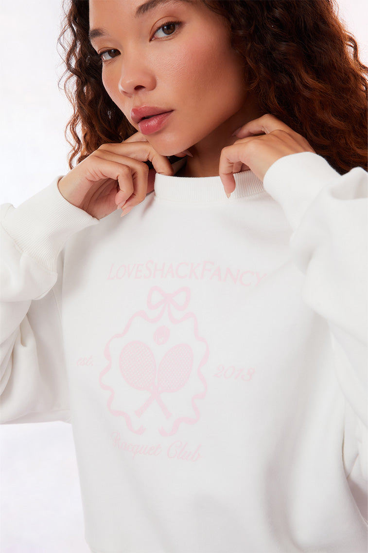 White pullover crew-neck sweater with ribbed sleeve cuffs, neckline, and hem. With a pink LoveShackFancy logo including two tennis raquets.