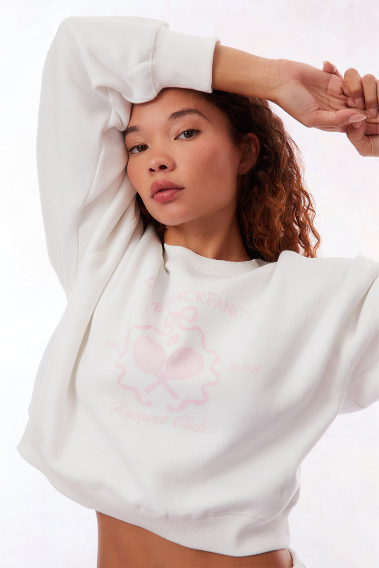 White pullover crew-neck sweater with ribbed sleeve cuffs, neckline, and hem. With a pink LoveShackFancy logo including two tennis raquets.