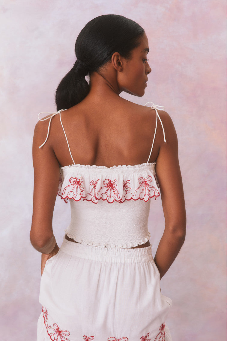 White organic cotton top with spaghetti straps that self tie. Smocked bodice with scalloped red cherry embroideries as a ruffle on the square neckline. Pairs with Amparo Skirt for a full set.