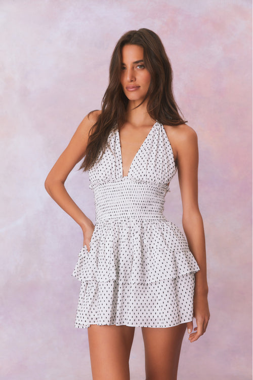 White low-cut v neck halter dress with black polka dots, halter ties in bow at neck and below, is a wide smocked waistband and the skirt has two ruffled tiers.