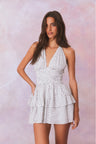 White low-cut v neck halter dress with black polka dots, halter ties in bow at neck and below, is a wide smocked waistband and the skirt has two ruffled tiers.