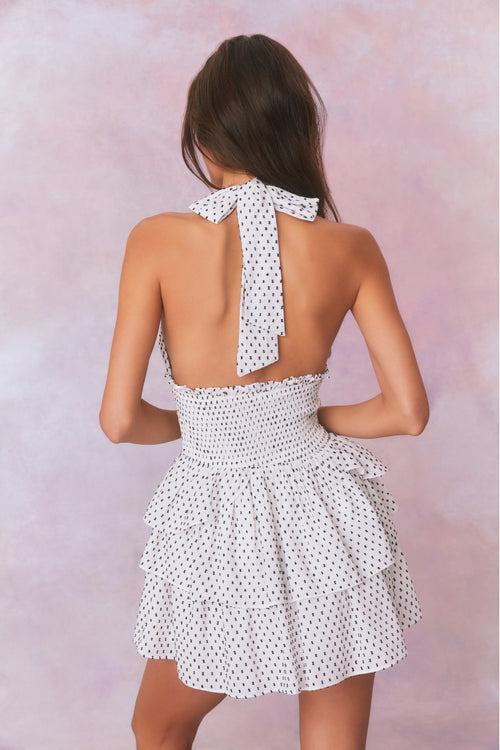 White low-cut v neck halter dress with black polka dots, halter ties in bow at neck and below, is a wide smocked waistband and the skirt has two ruffled tiers.