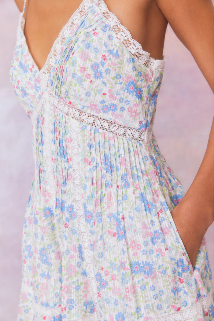 White mini dress with a blue floral pattern with lace insets and pintucking details, and features a smocked back, spaghetti straps, and an airy skirt finished with lace.