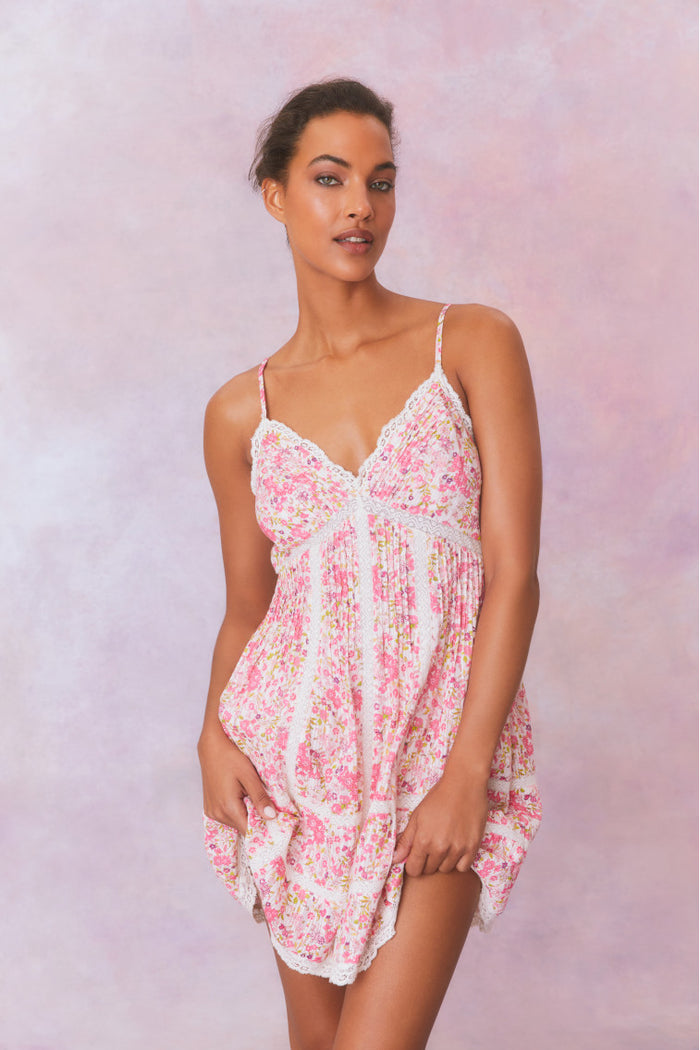 White mini dress with a pink floral pattern with lace insets and pintucking details, and features a smocked back, spaghetti straps, and an airy skirt finished with lace.