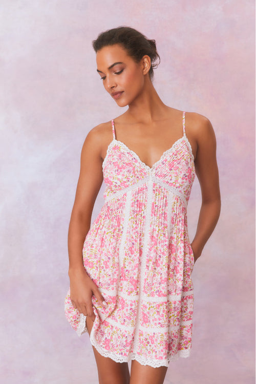 White mini dress with a pink floral pattern with lace insets and pintucking details, and features a smocked back, spaghetti straps, and an airy skirt finished with lace.