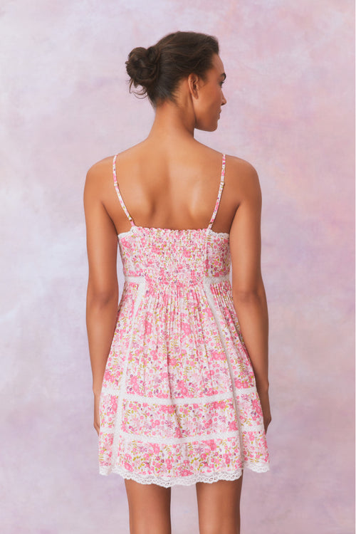 White mini dress with a pink floral pattern with lace insets and pintucking details, and features a smocked back, spaghetti straps, and an airy skirt finished with lace.