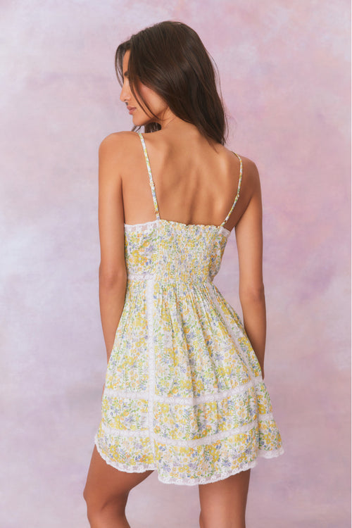 White mini dress with a yellow floral pattern with lace insets and pintucking details, and features a smocked back, spaghetti straps, and an airy skirt finished with lace.