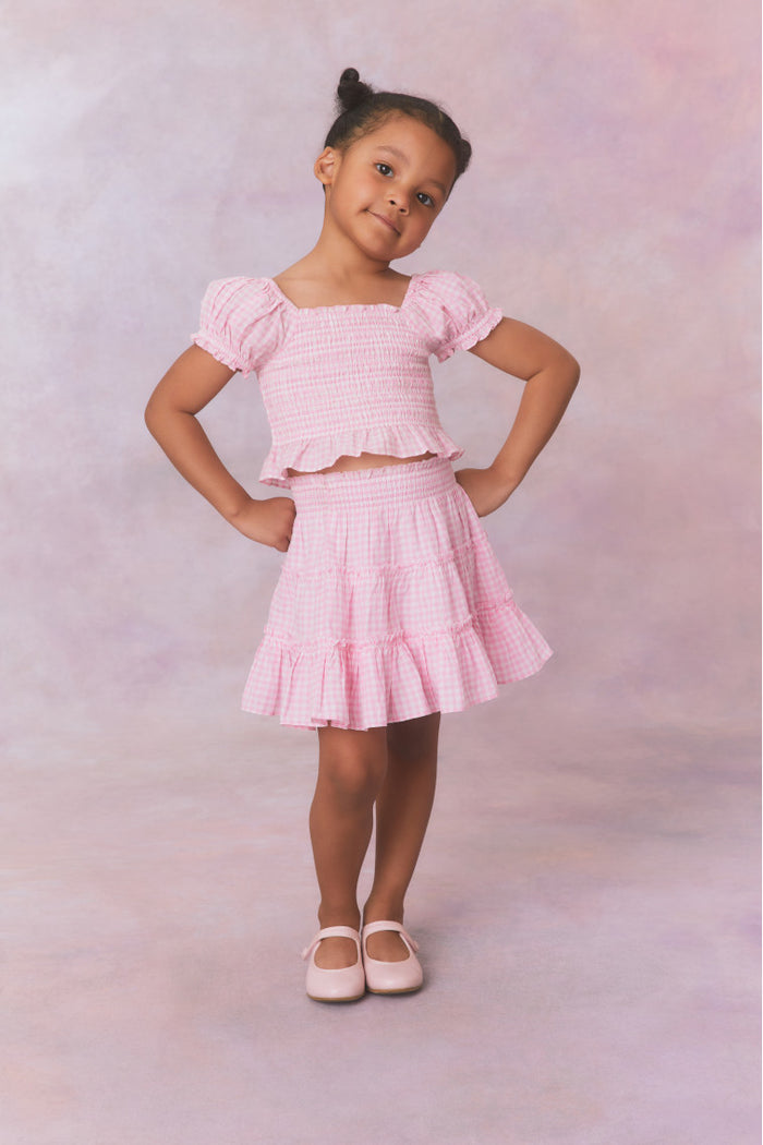 Pink gingham cotton off the shoulder top with puff sleeves and a smocked bodice flowing to a peplum finish for girls.