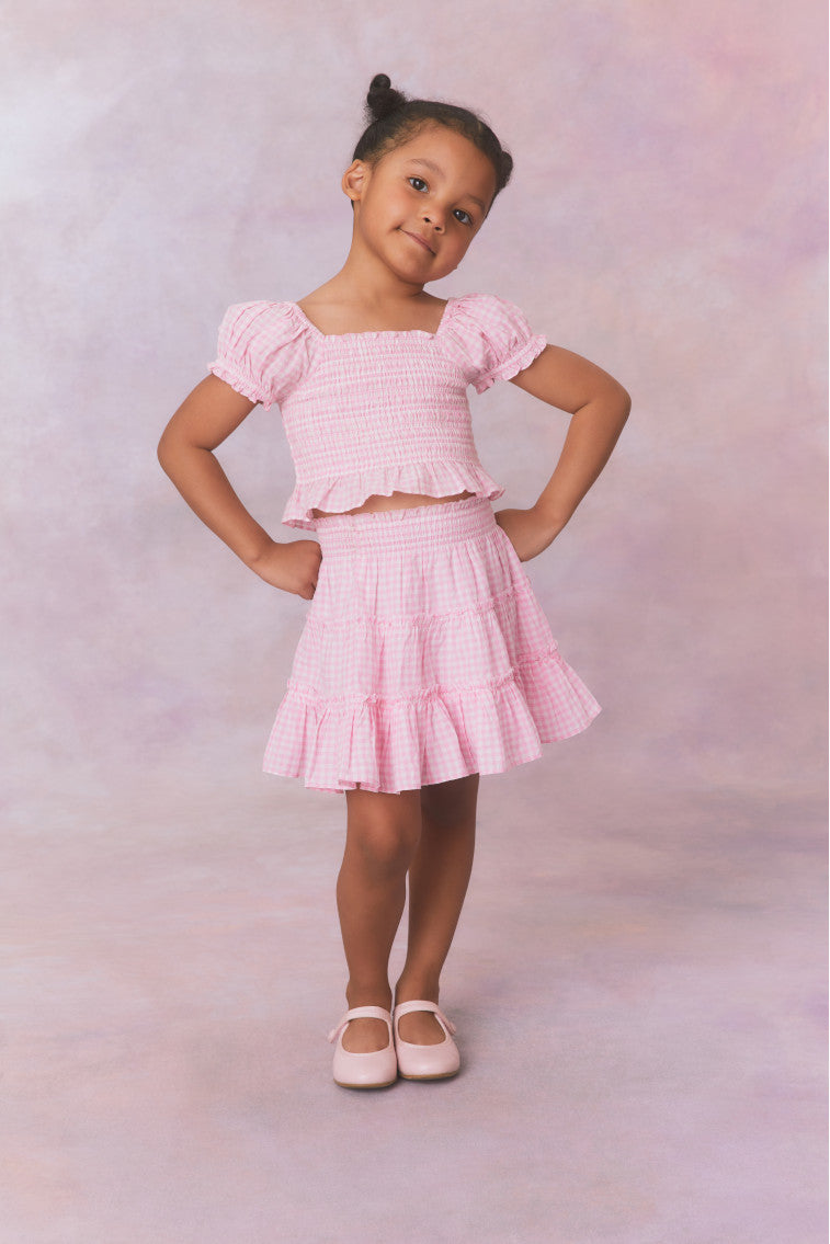 Pink gingham cotton off the shoulder top with puff sleeves and a smocked bodice flowing to a peplum finish for girls.