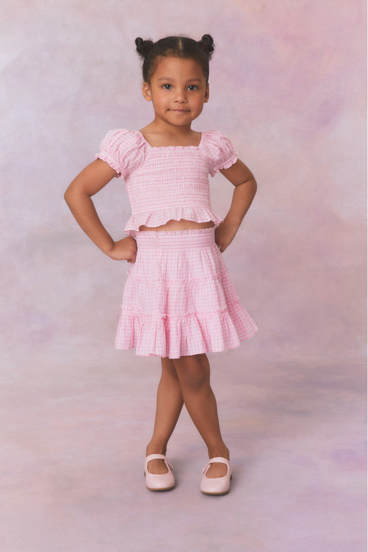 Pink gingham cotton off the shoulder top with puff sleeves and a smocked bodice flowing to a peplum finish for girls.