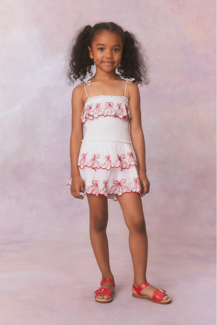 Girls white airy cotton tank with spaghetti bow straps, featuring cherry embroideries on a ruffle tier.