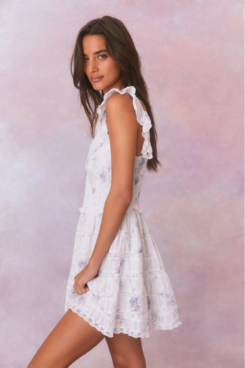 White mini dress with blue/purple floral details and an open v-neck with elasticated flutter sleeves and a smocked waist, the bodice and skirt contain lace and embroidery and is complete with pockets.