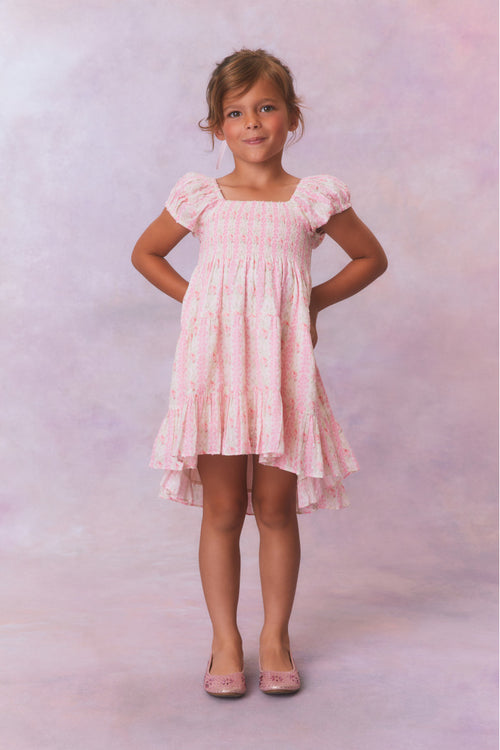 Pink floral dress for girls with flutter sleeves, a smocked top and ruffled skirt with an asymmetrical hem.