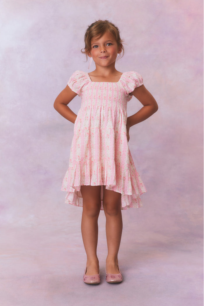 Pink floral dress for girls with flutter sleeves, a smocked top and ruffled skirt with an asymmetrical hem.