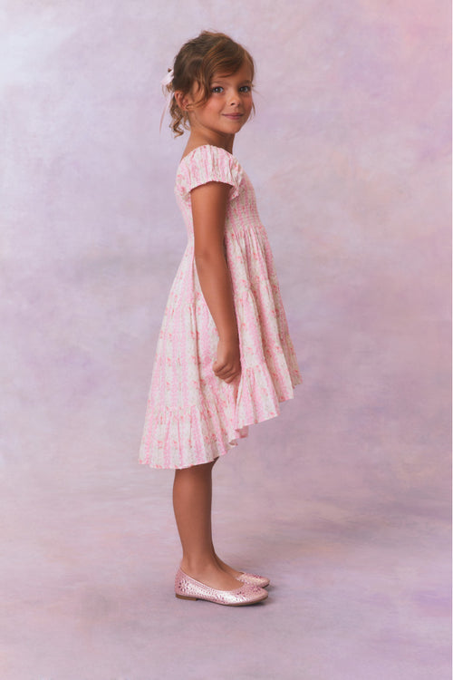 Pink floral dress for girls with flutter sleeves, a smocked top and ruffled skirt with an asymmetrical hem.