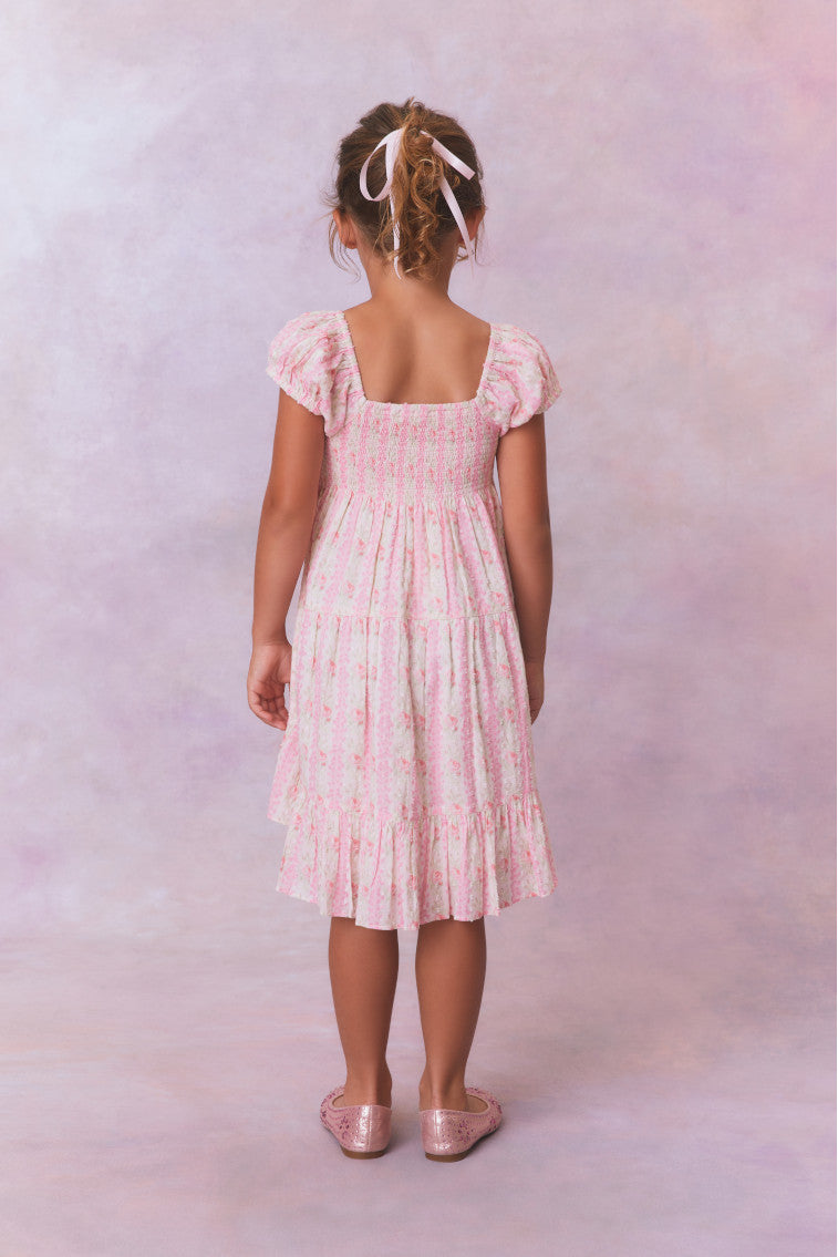 Pink floral dress for girls with flutter sleeves, a smocked top and ruffled skirt with an asymmetrical hem.