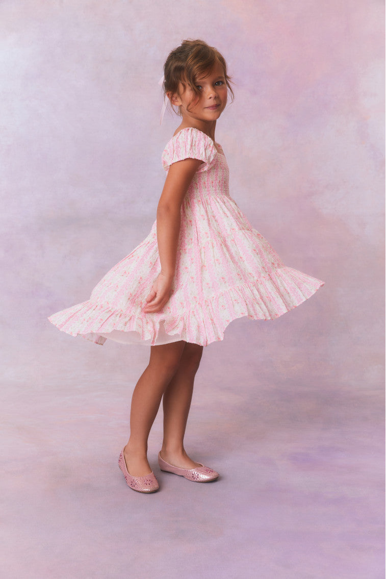 Pink floral dress for girls with flutter sleeves, a smocked top and ruffled skirt with an asymmetrical hem.