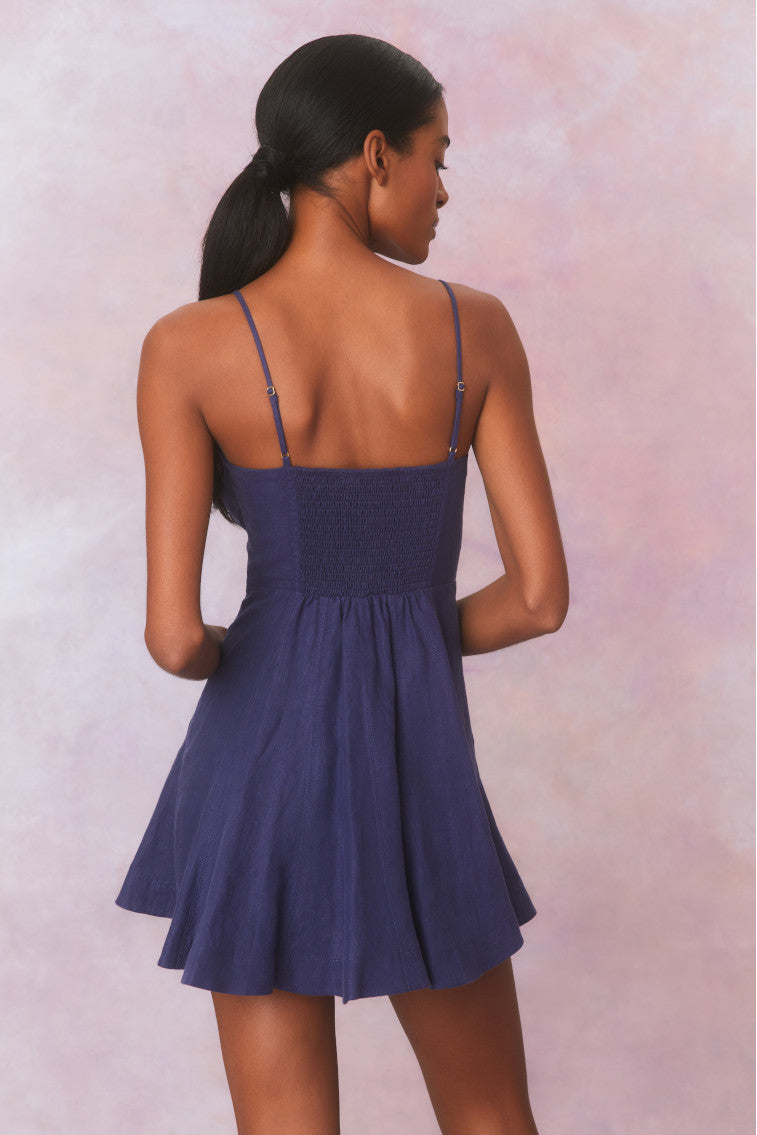 Navy mini dress with princess seams down the waistline that releases into a full sweepy skirt. Includes a smocked back, cups with shirring details.