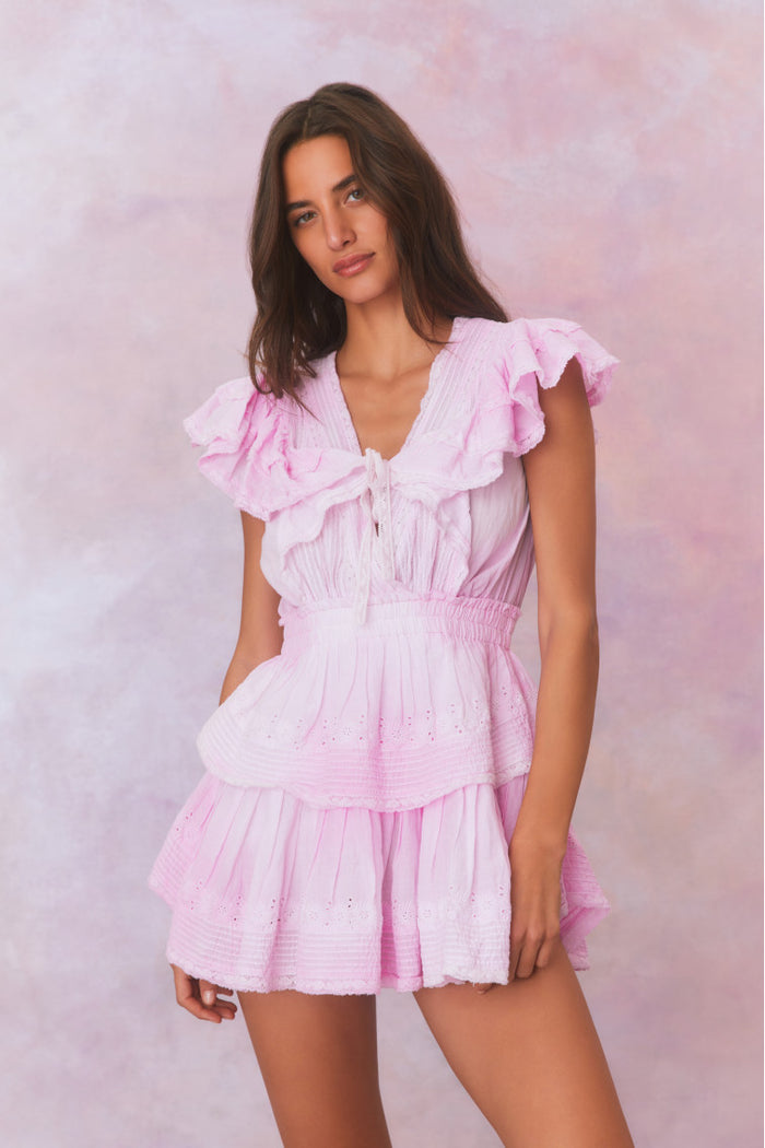 Pink hand-dyed cotton dress with lace embroidery details. Dress has a deep v neckline with ruffles on the outer edges of the shoulder and the bodice has an elastic waist and two flounced tiers.