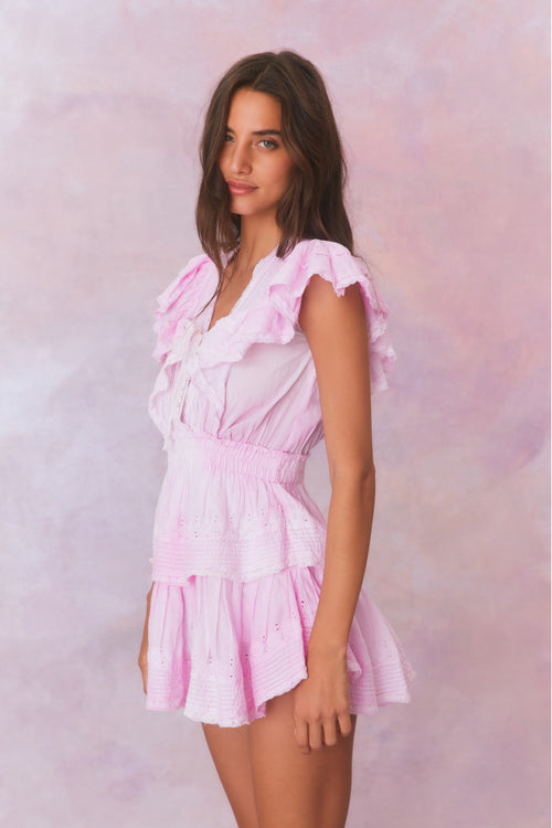 Pink hand-dyed cotton dress with lace embroidery details. Dress has a deep v neckline with ruffles on the outer edges of the shoulder and the bodice has an elastic waist and two flounced tiers.