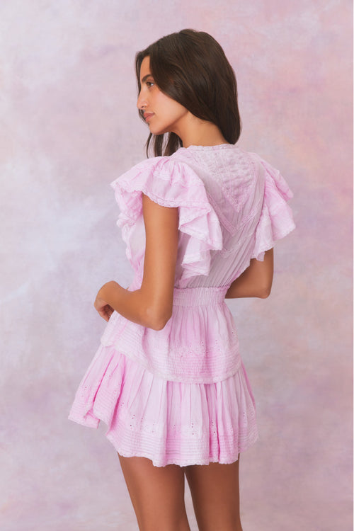 Pink hand-dyed cotton dress with lace embroidery details. Dress has a deep v neckline with ruffles on the outer edges of the shoulder and the bodice has an elastic waist and two flounced tiers.