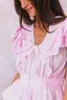 Pink hand-dyed cotton dress with lace embroidery details. Dress has a deep v neckline with ruffles on the outer edges of the shoulder and the bodice has an elastic waist and two flounced tiers.